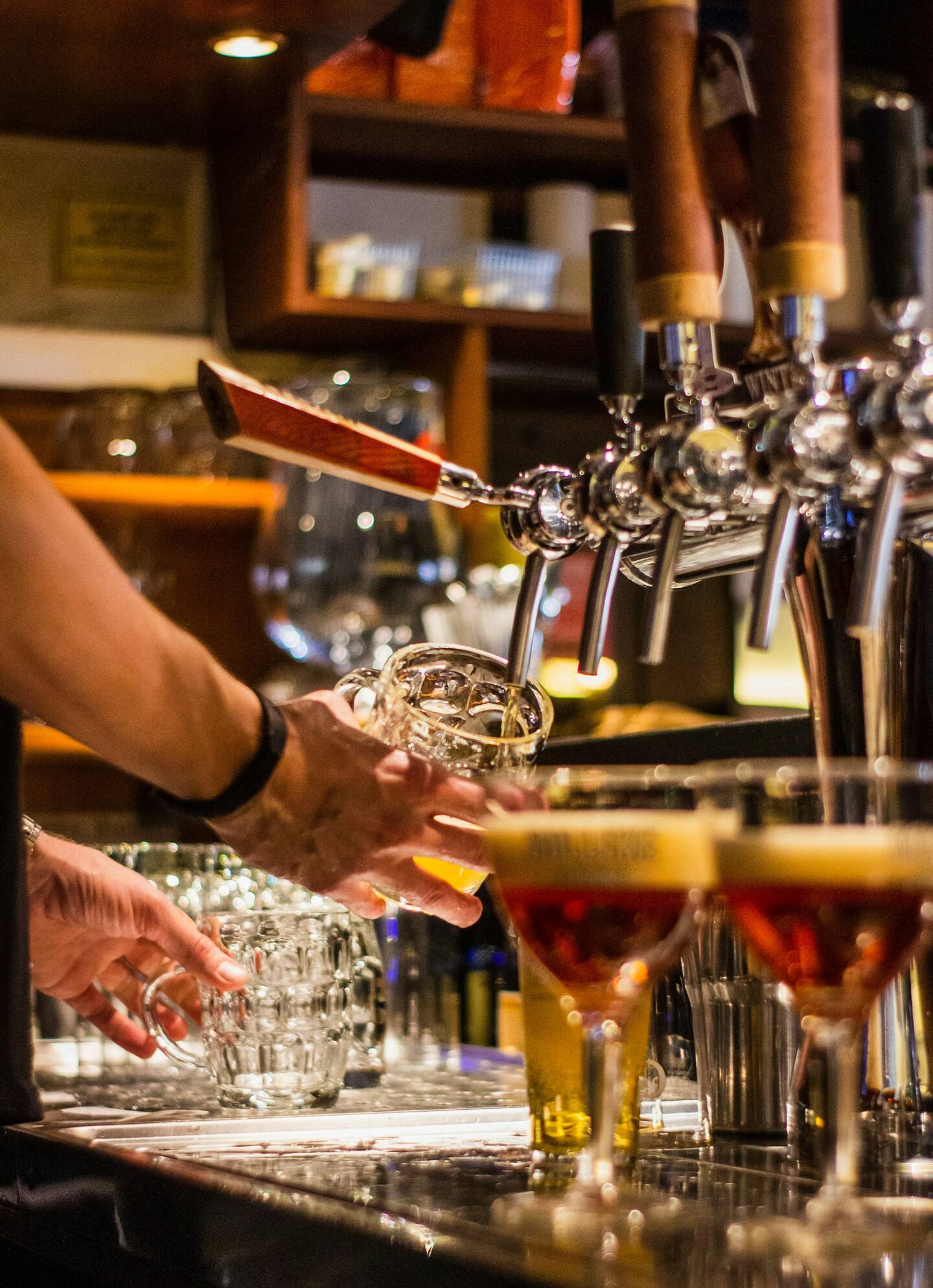 Bartender pulling a golden draft beer from a tap with warm overhead lighting.