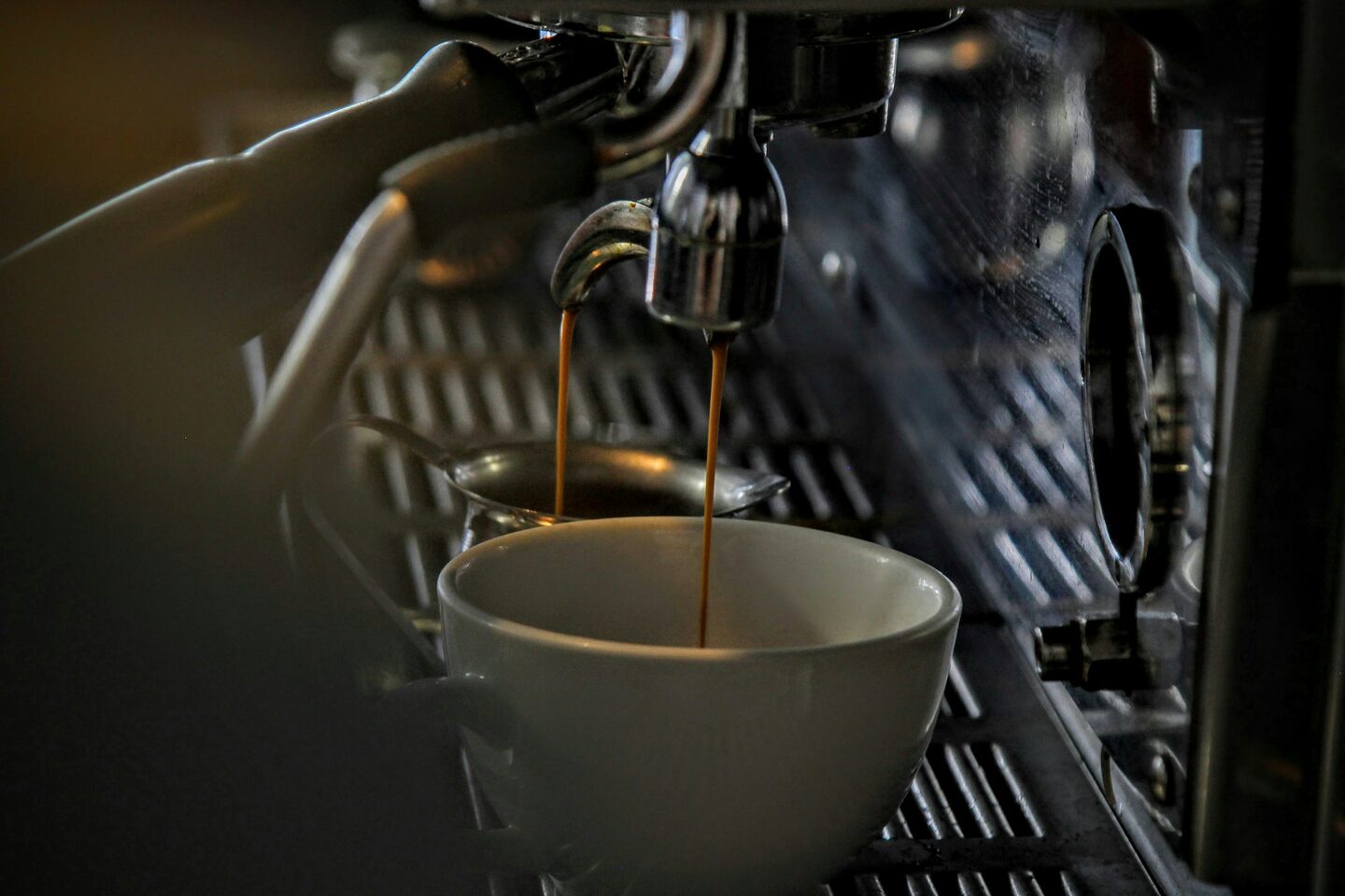 An espresso machine pulling a shot into a small white cup with soft morning steam rising.