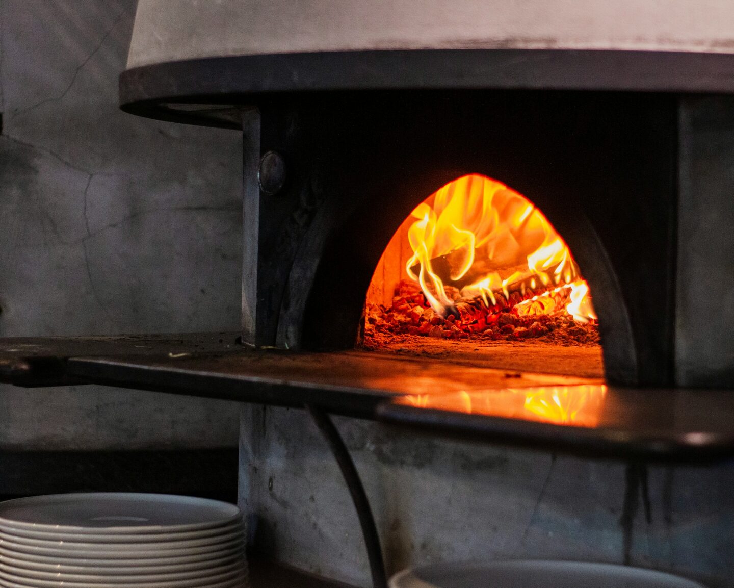 A wood-fired pizza coming out of the oven, hands holding the peel.