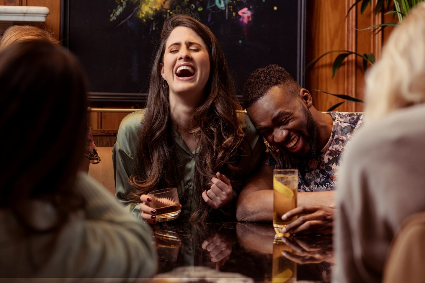 Friends laughing around a high-top with drinks and plates of food.