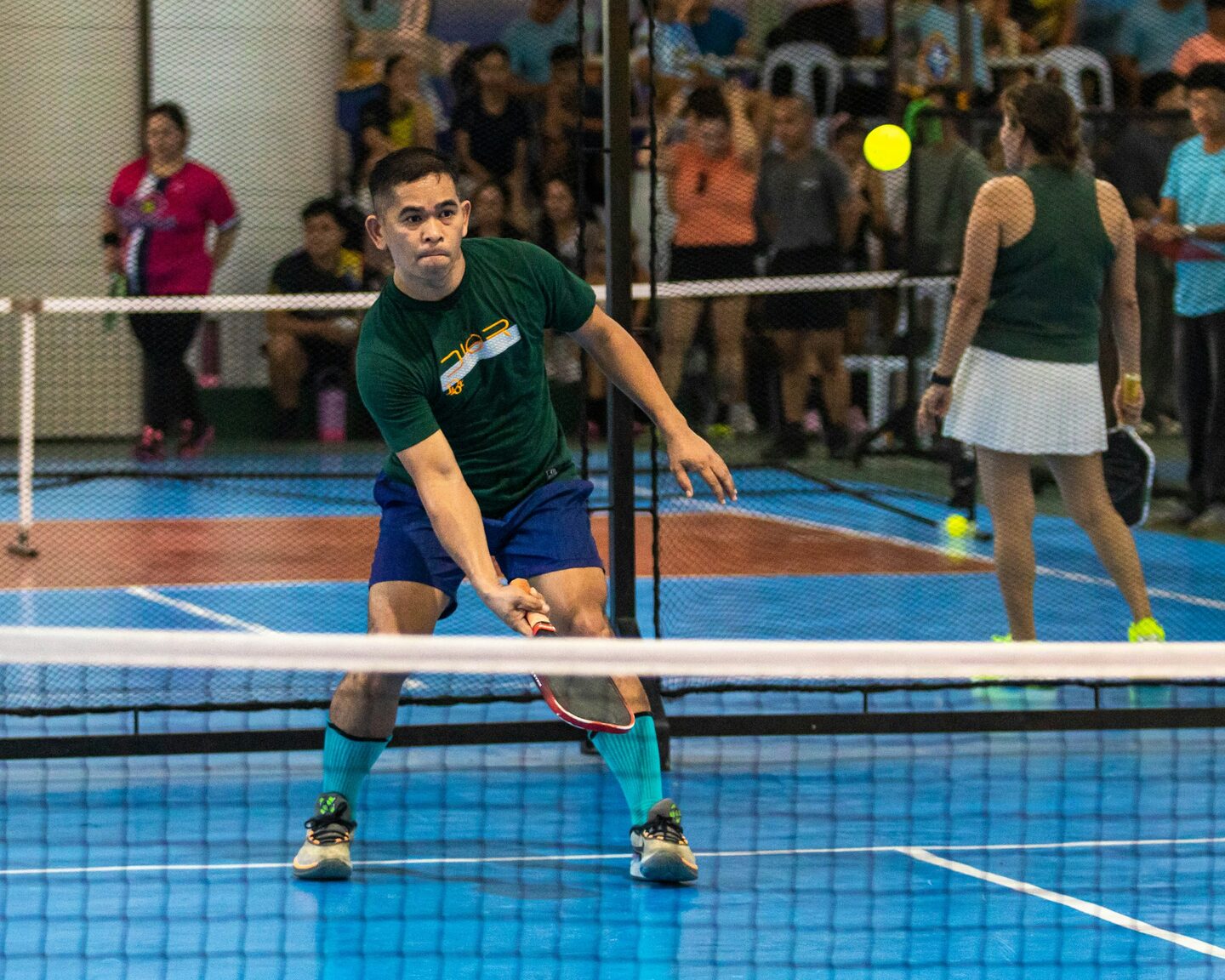 Indoor pickleball court mid-rally with warm overhead light.