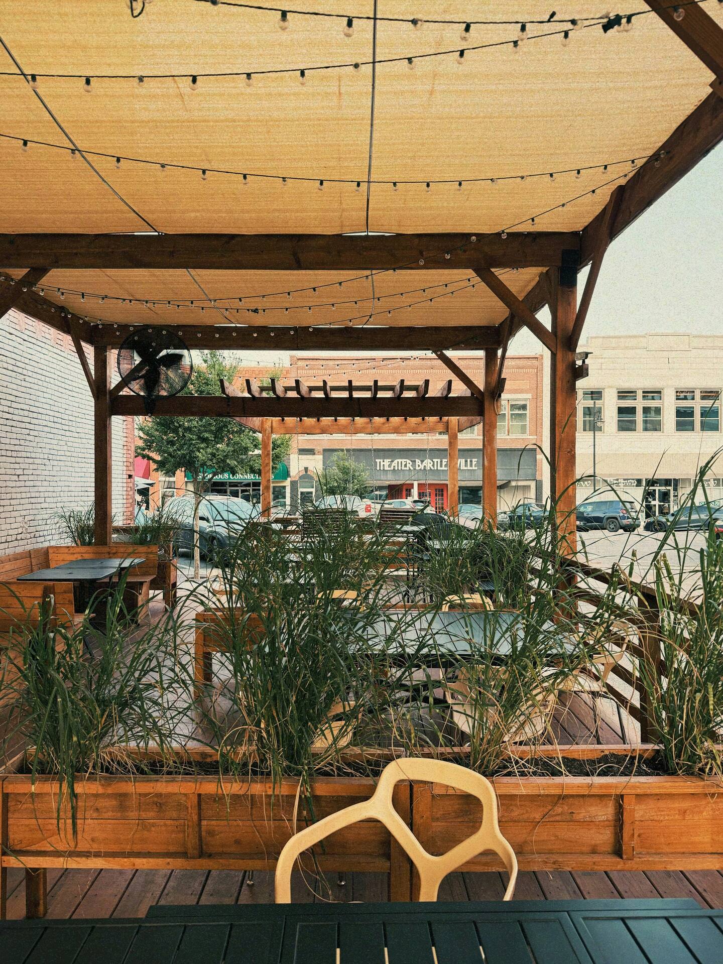 Wood pergola in soft evening light with hanging bulbs over a small bistro table.