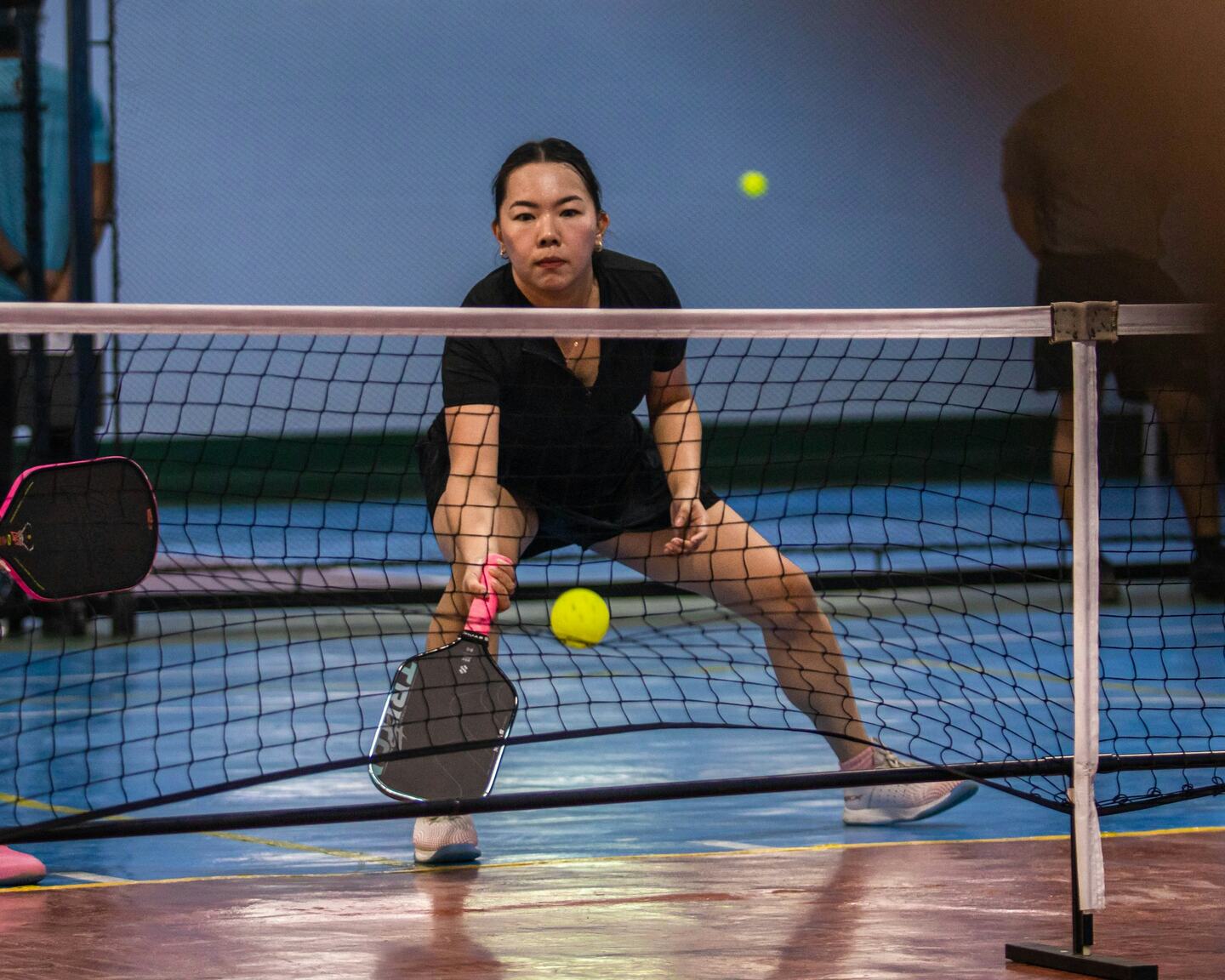 Indoor pickleball court mid-rally with warm overhead light.